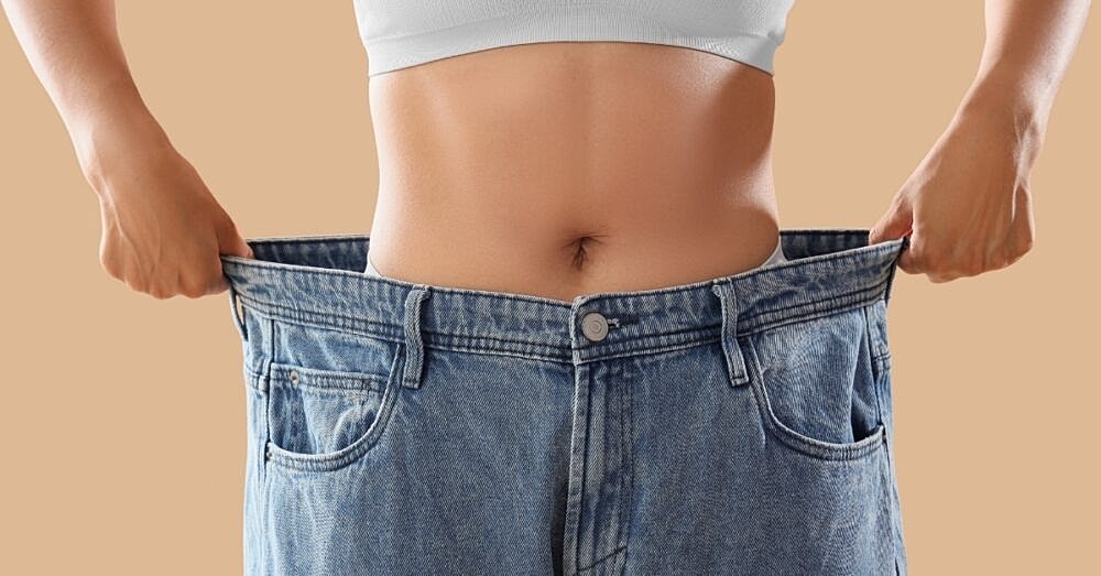 Person holding oversized jeans, showcasing weight loss.