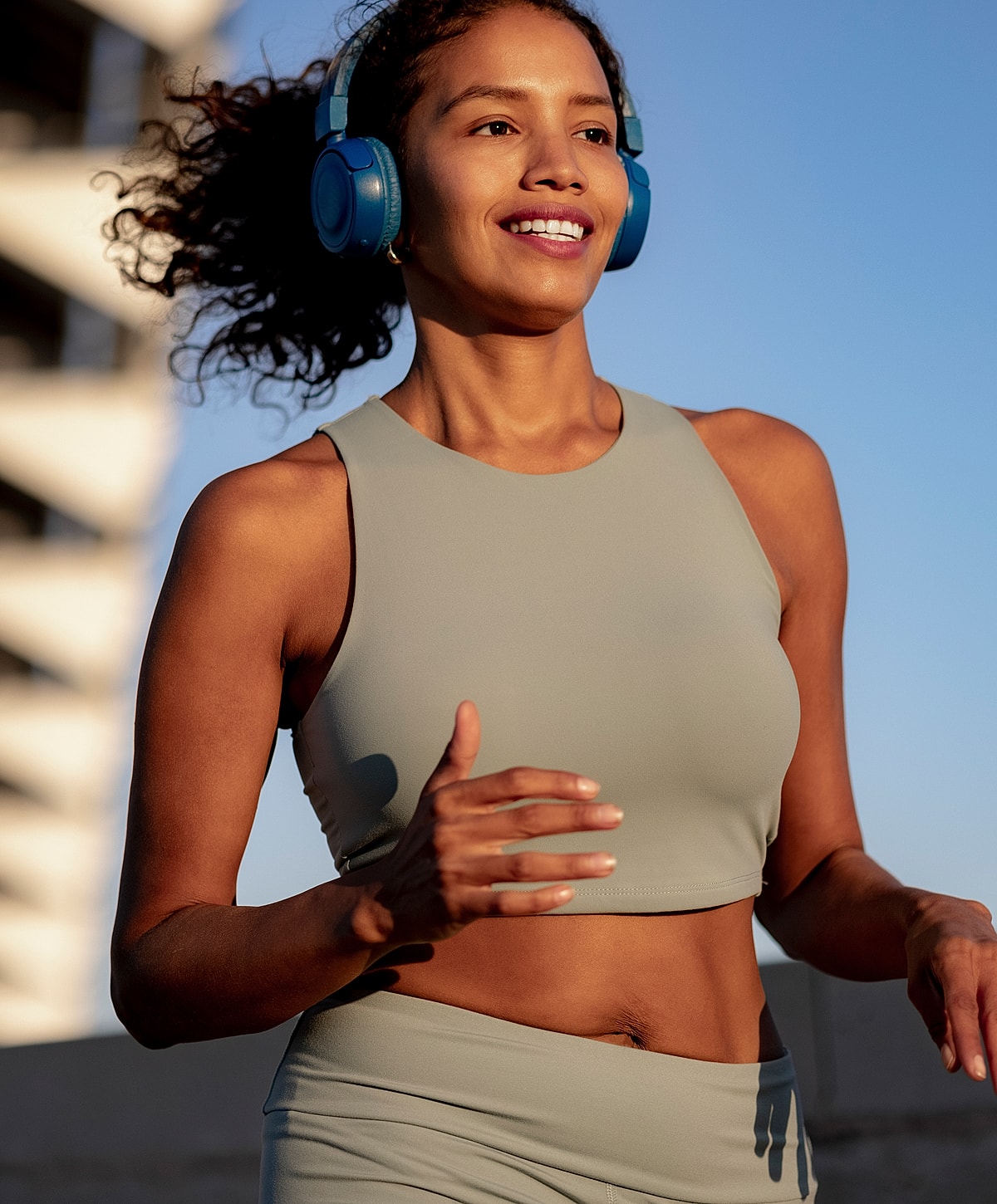 Woman jogging outdoors wearing headphones and activewear.