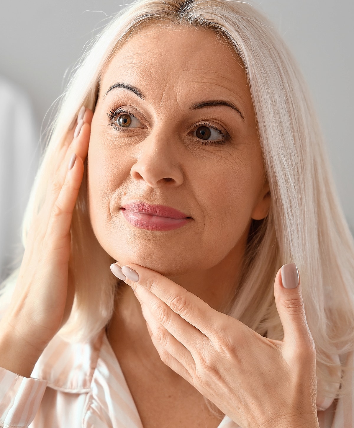 Woman examines her skin with gentle touch.