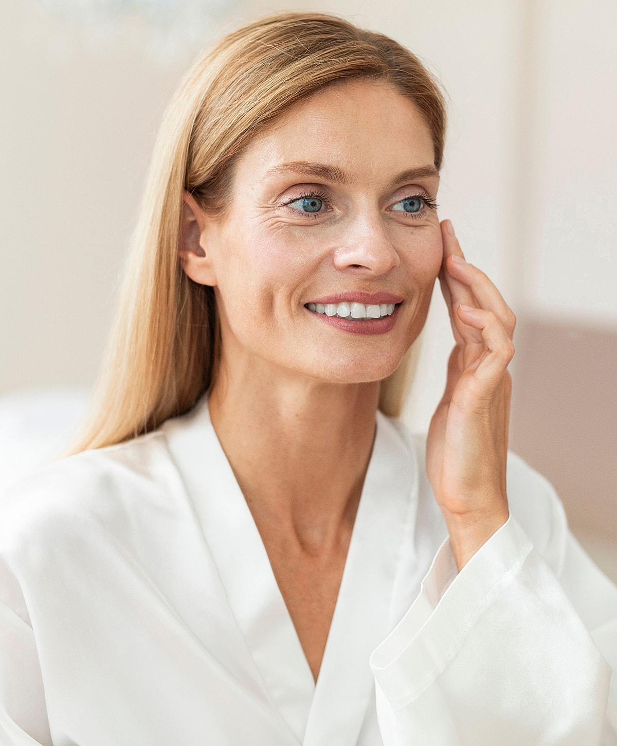 Woman in robe applying skincare product on face.
