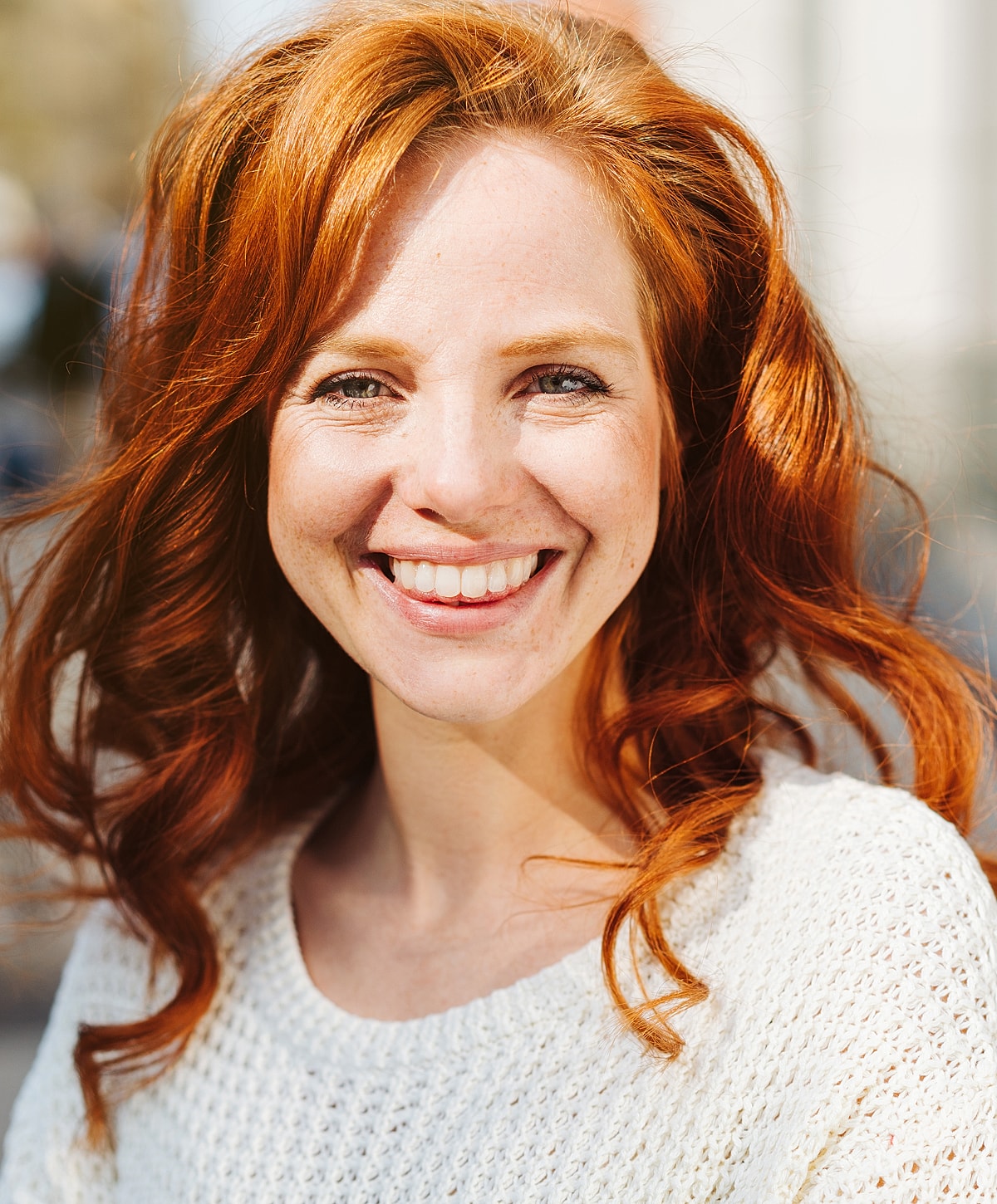 Smiling woman with red hair in white sweater.