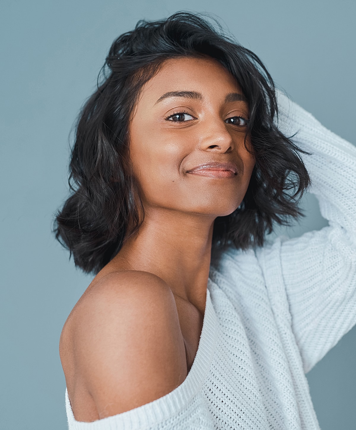 Smiling person in a light sweater against blue background.