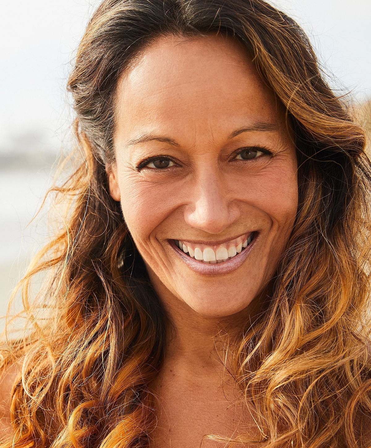Smiling woman with long, wavy hair outdoors.