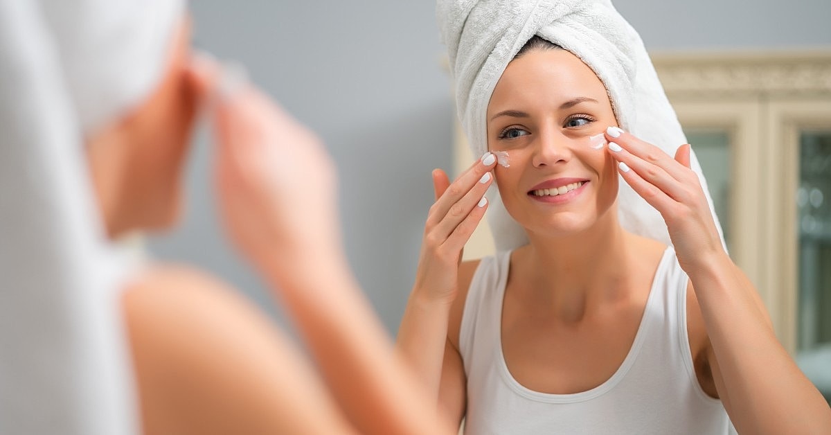 Woman applying skincare in bathroom mirror.