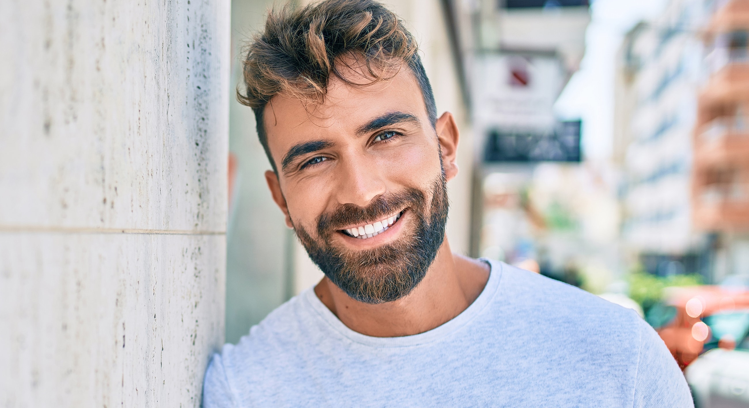 Smiling man leaning against a wall outdoors.